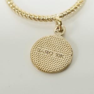 May include: A gold-colored necklace with a twisted chain and a round pendant. The pendant has a textured surface and the text "SARO 10K" inscribed on it.