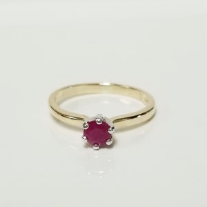 May include: A gold ring with a single red ruby gemstone set in a prong setting.