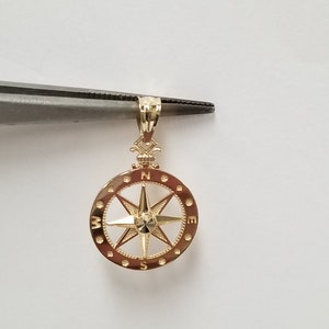 May include: Gold compass pendant with a detailed design. The compass features a star-shaped pointer and the letters N, S, E, and W around the edge.