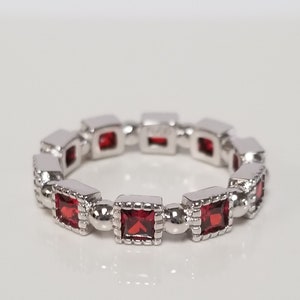 May include: A silver band ring with a row of red square-shaped gemstones.