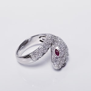 Op de afbeelding: Een zilveren ring met een slangendesign. De slang is bezet met heldere stenen en heeft een rode steen als oog.