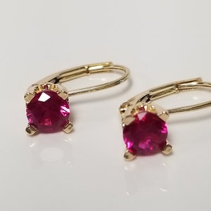 May include: A pair of gold hoop earrings with a single red gemstone in each hoop.