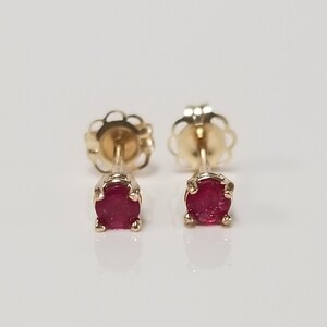 May include: A pair of gold stud earrings with small, round, red ruby gemstones.