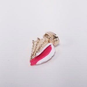 May include: Gold seashell pendant with pink and white enamel. The seashell has a detailed design and is a popular charm for jewelry making.