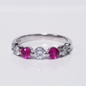 May include: A silver band ring with five round gemstones. Two red rubies are on either side of a larger, clear diamond.