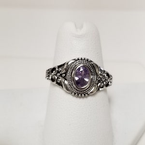 May include: A silver ring with an oval-shaped amethyst gemstone set in a detailed filigree design.