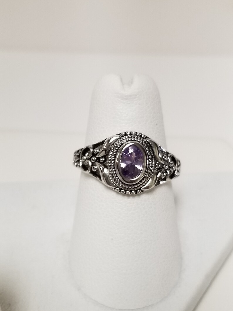 May include: A silver ring with an oval-shaped amethyst gemstone set in a detailed filigree design.