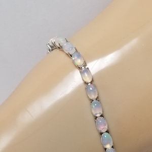 May include: A silver bracelet with oval-shaped white opals. The bracelet is made of a delicate chain and features a clasp closure.