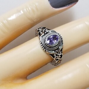 May include: A silver ring with an ornate design and a purple gemstone.