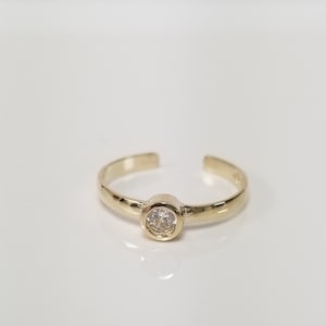 May include: A gold toe ring with a single clear round stone.