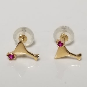 May include: A pair of gold earrings shaped like martini glasses with a small pink gemstone on each earring.