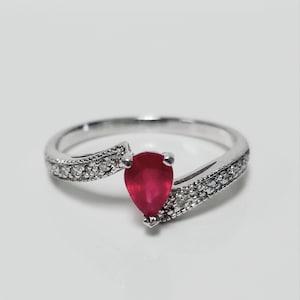 May include: A silver ring with a pear-shaped red ruby gemstone and a band of small diamonds.