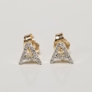 May include: A pair of gold earrings with a diamond-encrusted letter 'A' on each earring.