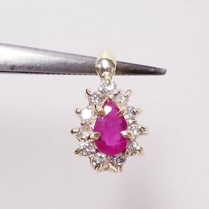 May include: A pear-shaped ruby pendant set in gold with a halo of small diamonds.