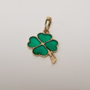 May include: A gold-colored pendant featuring a four-leaf clover design. The clover's leaves are a vibrant green, outlined in gold. The pendant has a small loop for a chain and a textured stem.