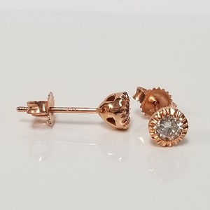 May include: A pair of rose gold stud earrings with a single round diamond in each earring.