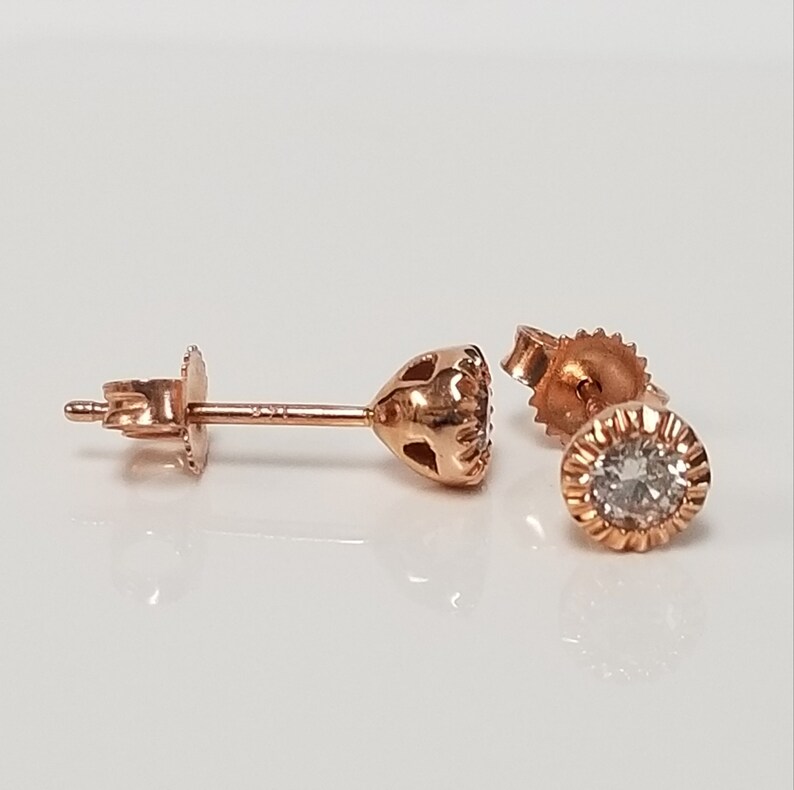 May include: A pair of rose gold stud earrings with a single round diamond in each earring.