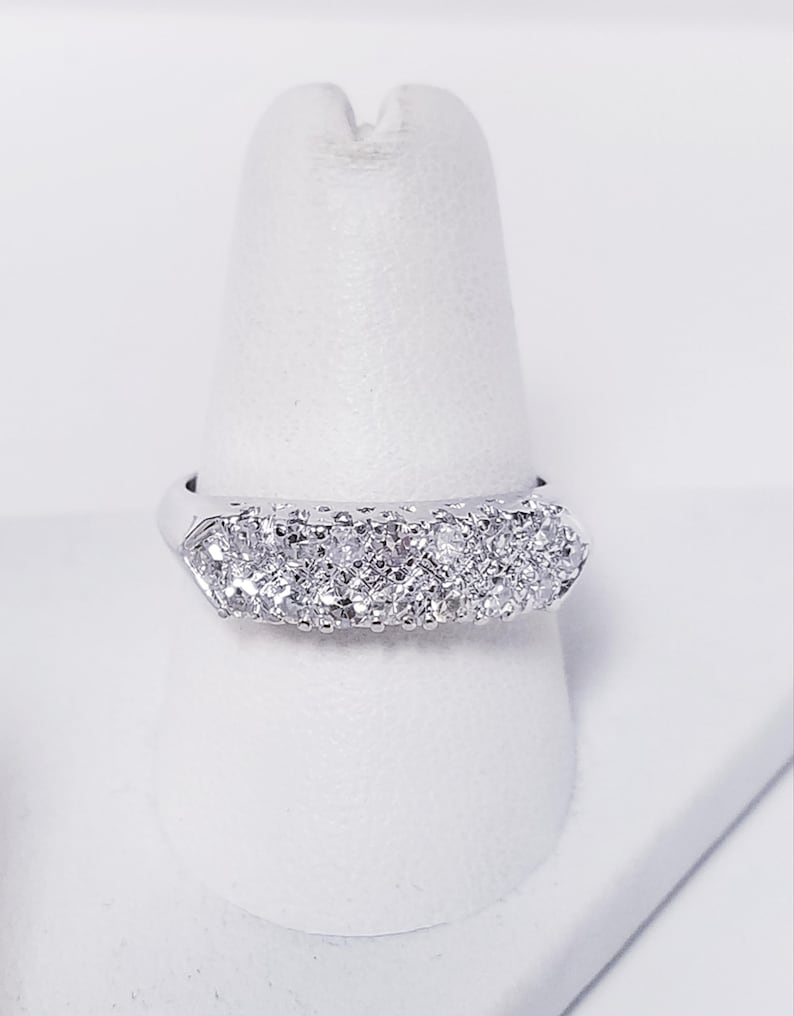 Op de afbeelding: Een zilveren bandring met een rij kleine, heldere diamanten in pav&eacute;-zetting.