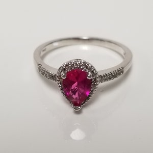 May include: A silver ring with a pear-shaped red gemstone surrounded by a halo of smaller white gemstones.