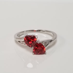 May include: A silver ring with two red heart-shaped gemstones. The ring has a delicate design with small clear stones on the band.