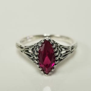 May include: A silver ring with a marquise-shaped ruby gemstone set in a filigree design.