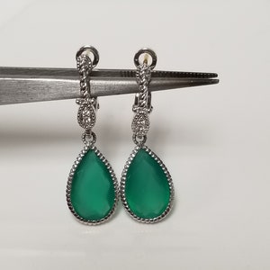 May include: A pair of silver teardrop earrings with green gemstone drops and a diamond-like accent on the top of each earring.