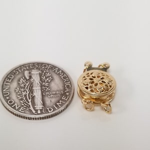 May include: Gold-toned metal clasp with a decorative filigree design. The clasp is about the size of a US dime.