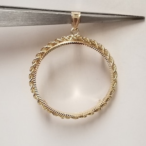 May include: A gold-toned coin pendant with a rope-like border. The pendant has a bail for attaching to a chain.