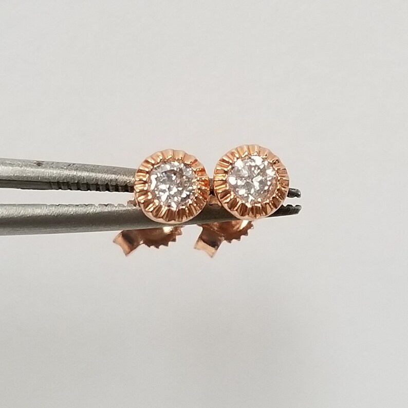May include: A pair of rose gold stud earrings with a small round diamond in the center of each earring.