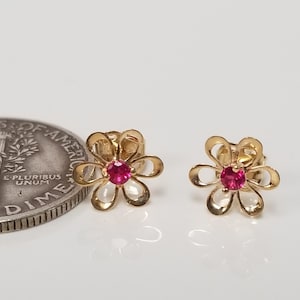 Op de afbeelding: Een paar gouden oorringen in de vorm van een bloem met een rode edelsteen in het midden van elke bloem.