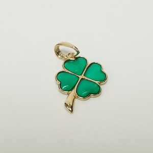 May include: A gold-colored pendant featuring a four-leaf clover design. The clover's four heart-shaped leaves are a vibrant green, outlined in gold. The pendant has a loop for a chain and a stem detail.
