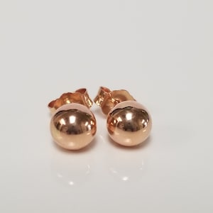 May include: A pair of rose gold ball stud earrings. The earrings are simple and elegant, and they would make a great gift for any occasion.