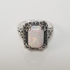 May include: A silver ring with an ornate design featuring a large, rectangular, iridescent opal gemstone.
