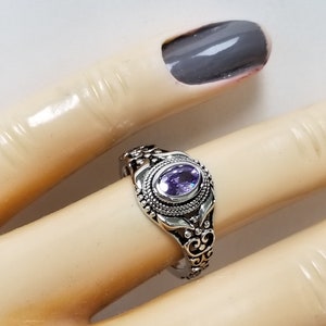 May include: A silver ring with an oval-shaped purple gemstone set in a filigree design.