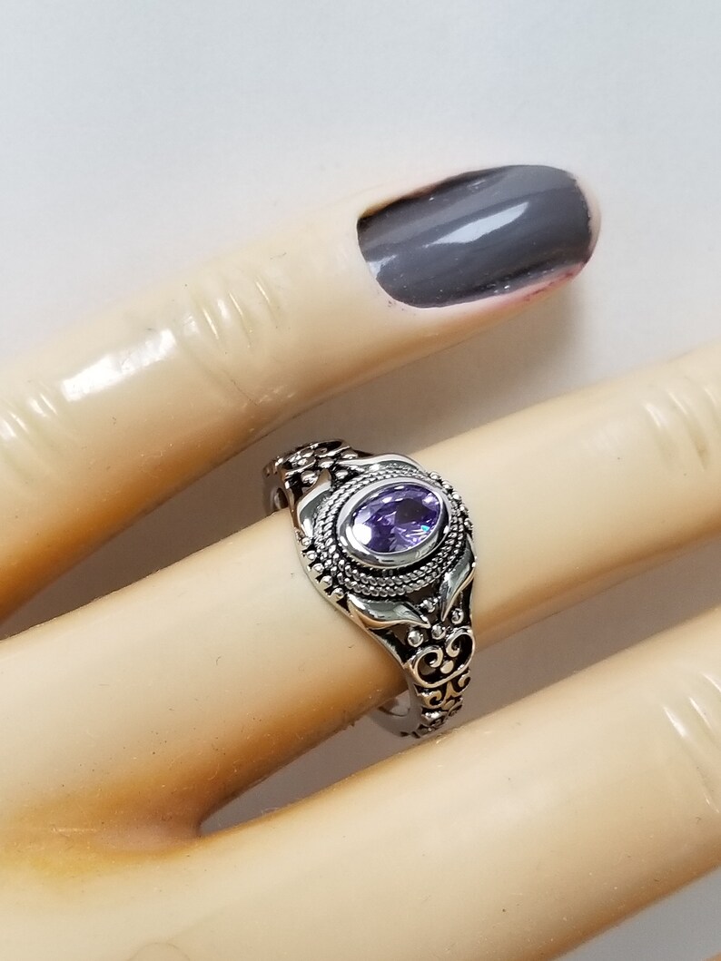 May include: A silver ring with an oval-shaped purple gemstone set in a filigree design.