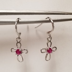 May include: A pair of silver hoop earrings with a dangling cross charm. Each cross has a small red gemstone in the center.