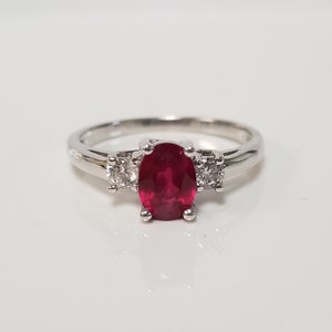 Peut inclure: Une bague en argent avec une pierre précieuse ovale en rubis rouge et deux diamants plus petits.