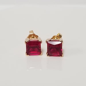 May include: A pair of gold earrings with square red ruby gemstones.