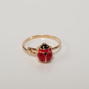 May include: A gold ring with a red ladybug design. The ladybug has black spots and a black head.