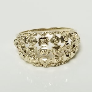 May include: A gold ring with an unusual openwork design. The ring has a series of square and rectangular cutouts, creating a textured, geometric pattern. The band is smooth, and the ring appears to be made of a shiny metal.