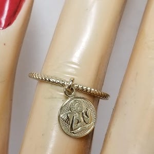 May include: A gold ring with a twisted band and a small charm of an angel with wings. The charm is round and has a detailed design.