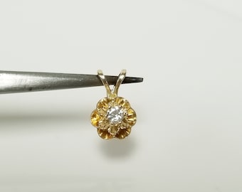 May include: A gold pendant shaped like a six-petaled flower with a single clear, round-cut gemstone set in the center. The pendant features a small, triangular bail at the top for attachment to a chain, showcasing a polished metallic finish.