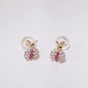 May include: A pair of gold-tone earrings featuring a ladybug design with clear and pink cubic zirconia stones.