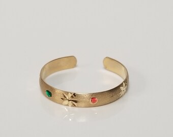 May include: A gold toe ring with a brushed finish and two small gemstones. One gemstone is green and the other is red.