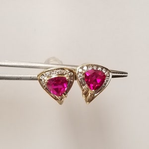 May include: A pair of gold earrings featuring a triangular ruby gemstone set within a halo of small diamonds.