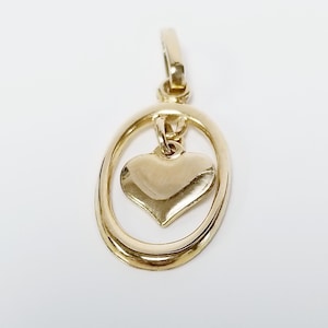 May include: A gold-colored pendant featuring a heart shape suspended within an oval frame. The pendant has a polished finish and a small loop at the top for attachment to a chain or bracelet. The jewelry is set against a white background.