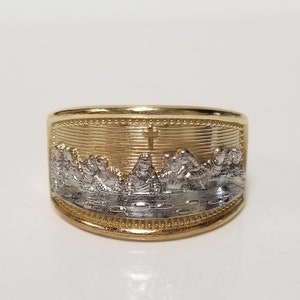 May include: A gold and silver ring with a depiction of the Last Supper. The ring is wide and has a textured band.
