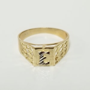 May include: A gold ring with a diamond-cut design and the letter "E" in the centre.
