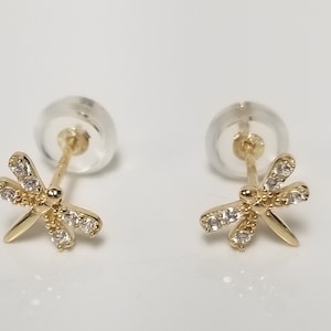 May include: A pair of gold dragonfly earrings with clear crystal accents. The earrings are stud style with a post and butterfly backing.