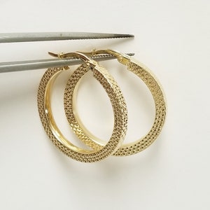 May include: A pair of gold hoop earrings with a textured surface.